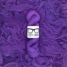 Load image into Gallery viewer, Purple yarn skein with a 'Feisty Fibres' label on a purple background