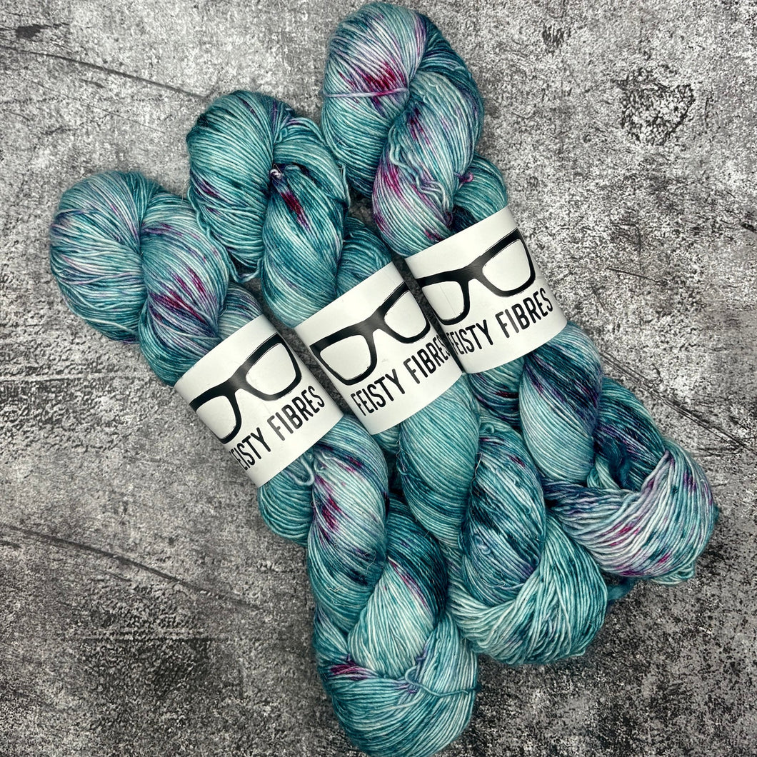 A skein of pink merino linen yarn with a label that reads 'Feisty Fibres', surrounded by unspooled yarn.