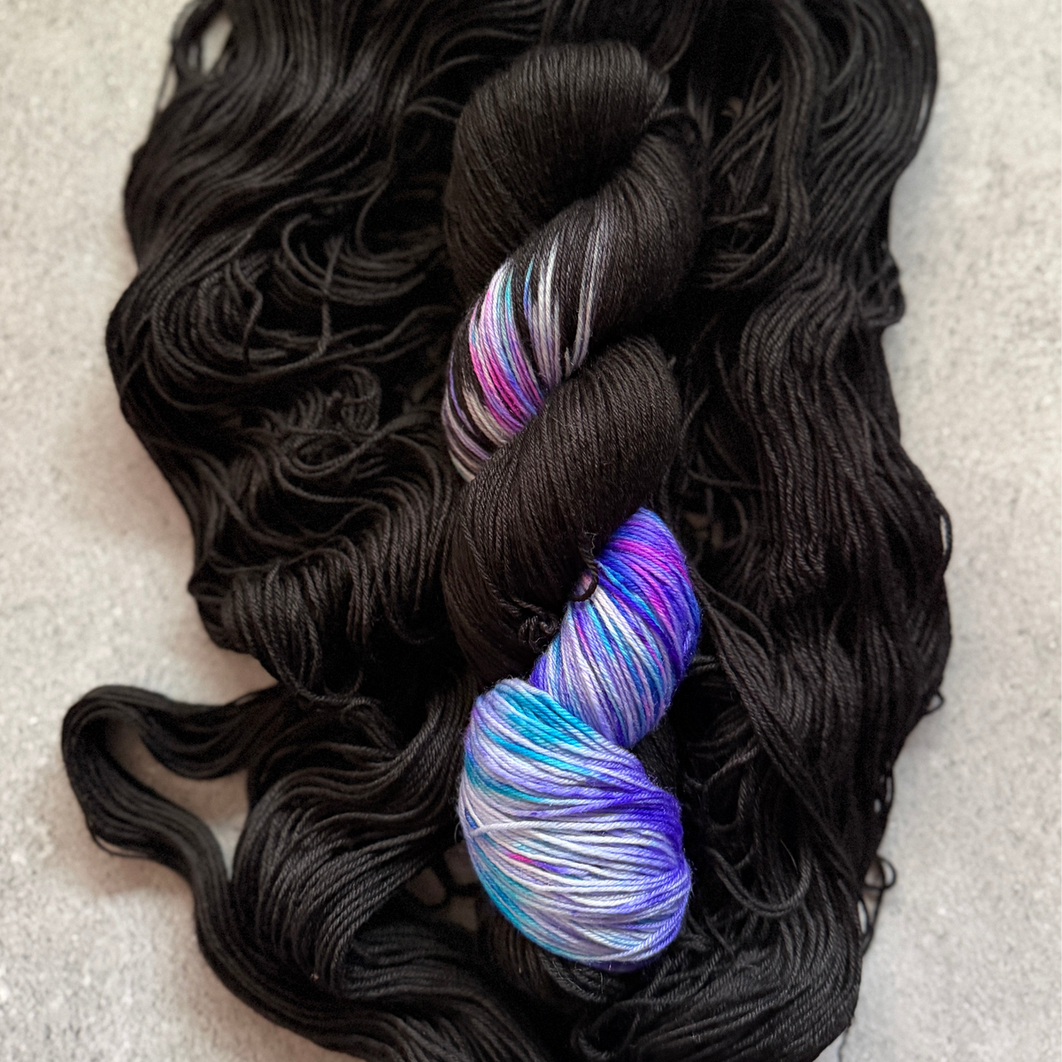 Two skeins of yarn, one black and one multicolored, on a textured surface.