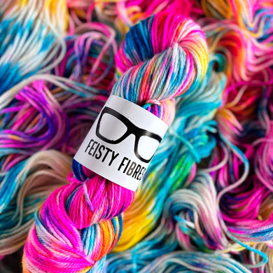 Florescent rainbow skein of yarn with a 'Feisty Fibres' label amidst more yarn.