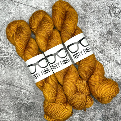 Three skeins of mustard yellow yarn with 'Tasty Fibres' labels on a gray textured background